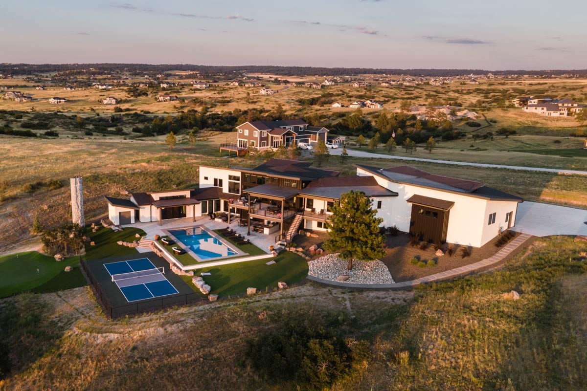 Modern house plan exterior with multiple gables, flat and sloped rooflines, large windows, and expansive patio overlooking pool.