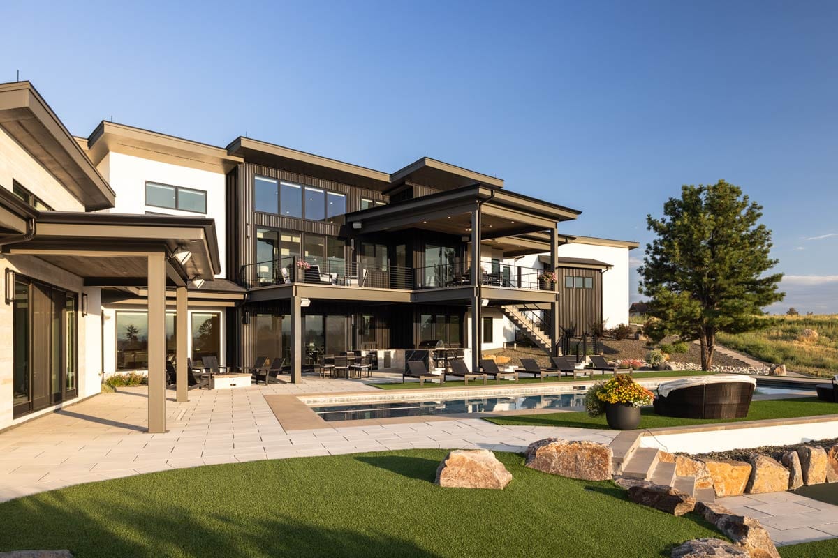 Modern multi-story house plan exterior with expansive windows, balconies, and covered patios overlooking a pool.