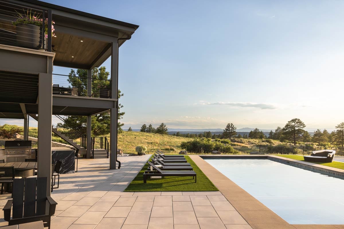 Modern house exterior with multi-level decks, outdoor kitchen, and infinity pool overlooking a scenic landscape.