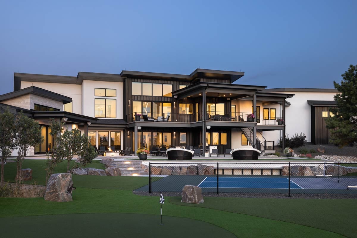 Modern house plan exterior with multiple levels, balconies, and large windows. Features a tiered backyard with a tennis court and putting green.