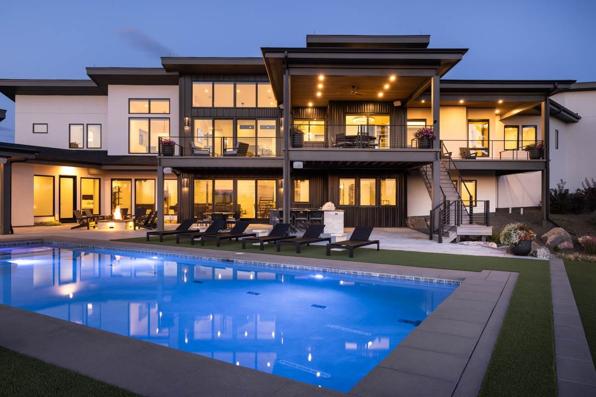Modern multi-story house plan exterior with multiple balconies, large windows, dark metal siding, and a swimming pool.