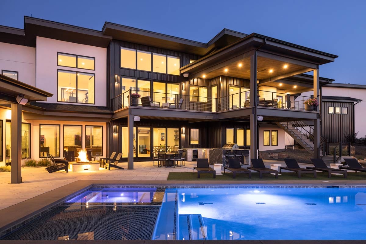 Modern house exterior with multiple levels, balconies, large windows, pool, and outdoor kitchen area.
