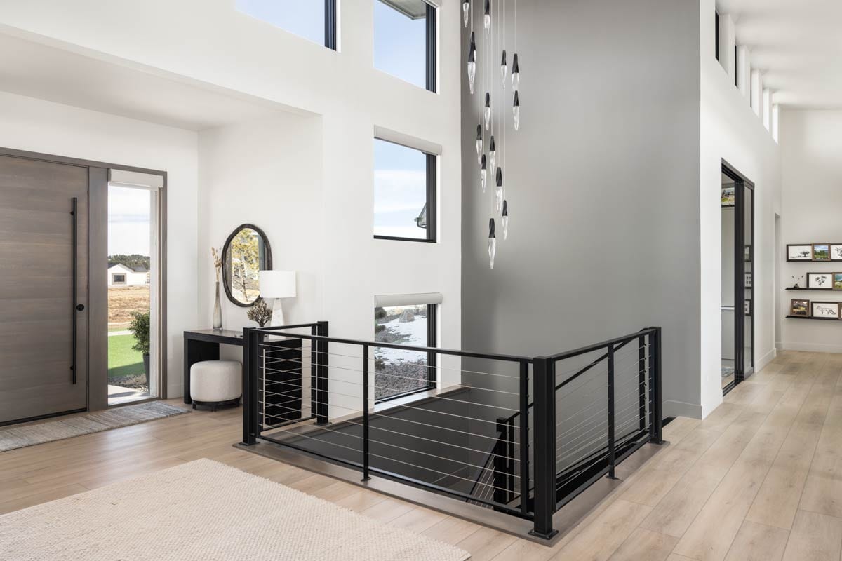 Modern entryway with high ceilings, clerestory windows, minimalist staircase with cable railing, and wood flooring.