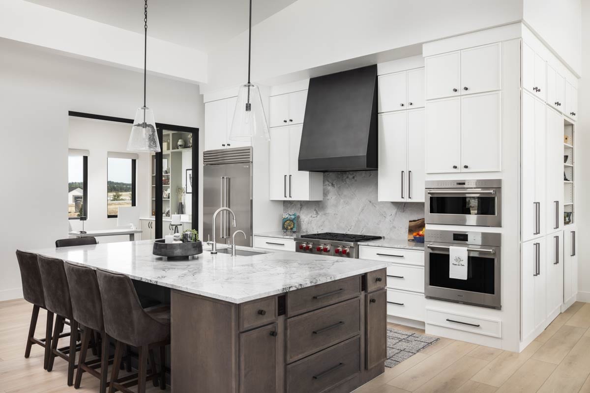 Modern kitchen with island seating, stainless steel appliances, white cabinetry, and a black range hood.