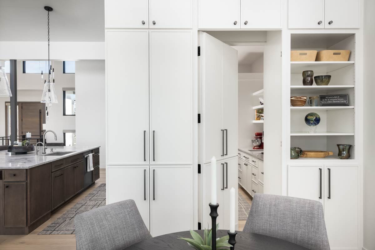 Modern kitchen with white cabinetry, island with sink, and a hidden pantry entrance.