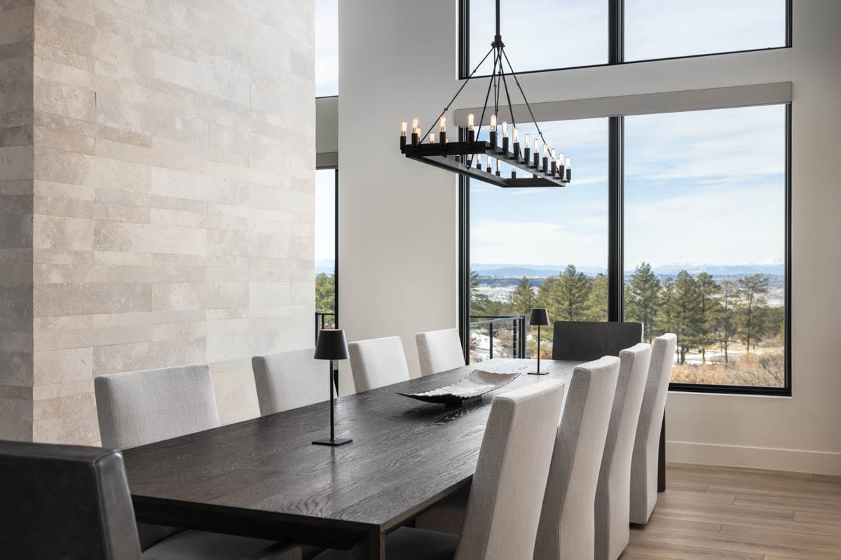 Interior view of dining room with dark wood table, upholstered chairs, stone accent wall, and large windows with scenic view.
