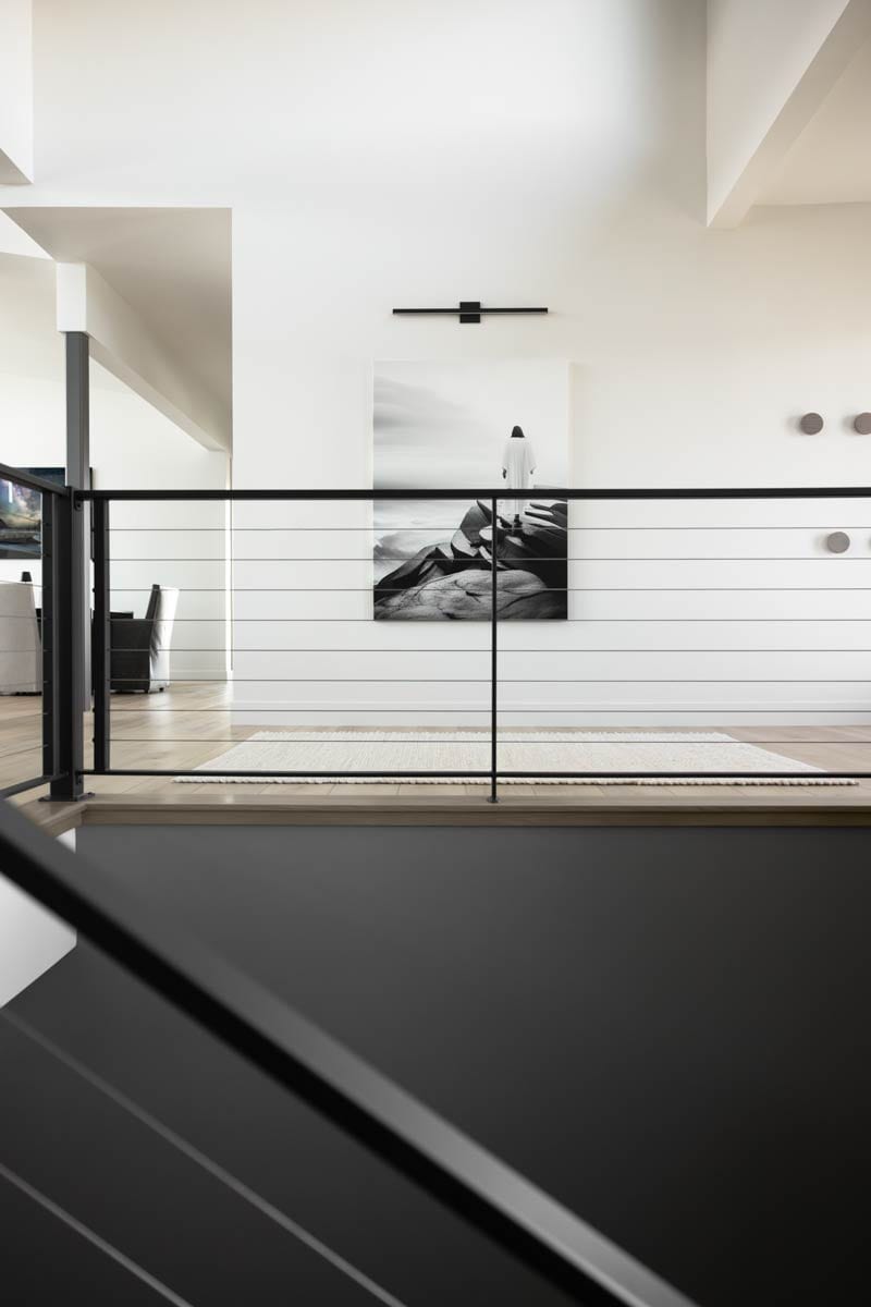 Interior view: hallway with modern art, horizontal railing, and light wood floors.